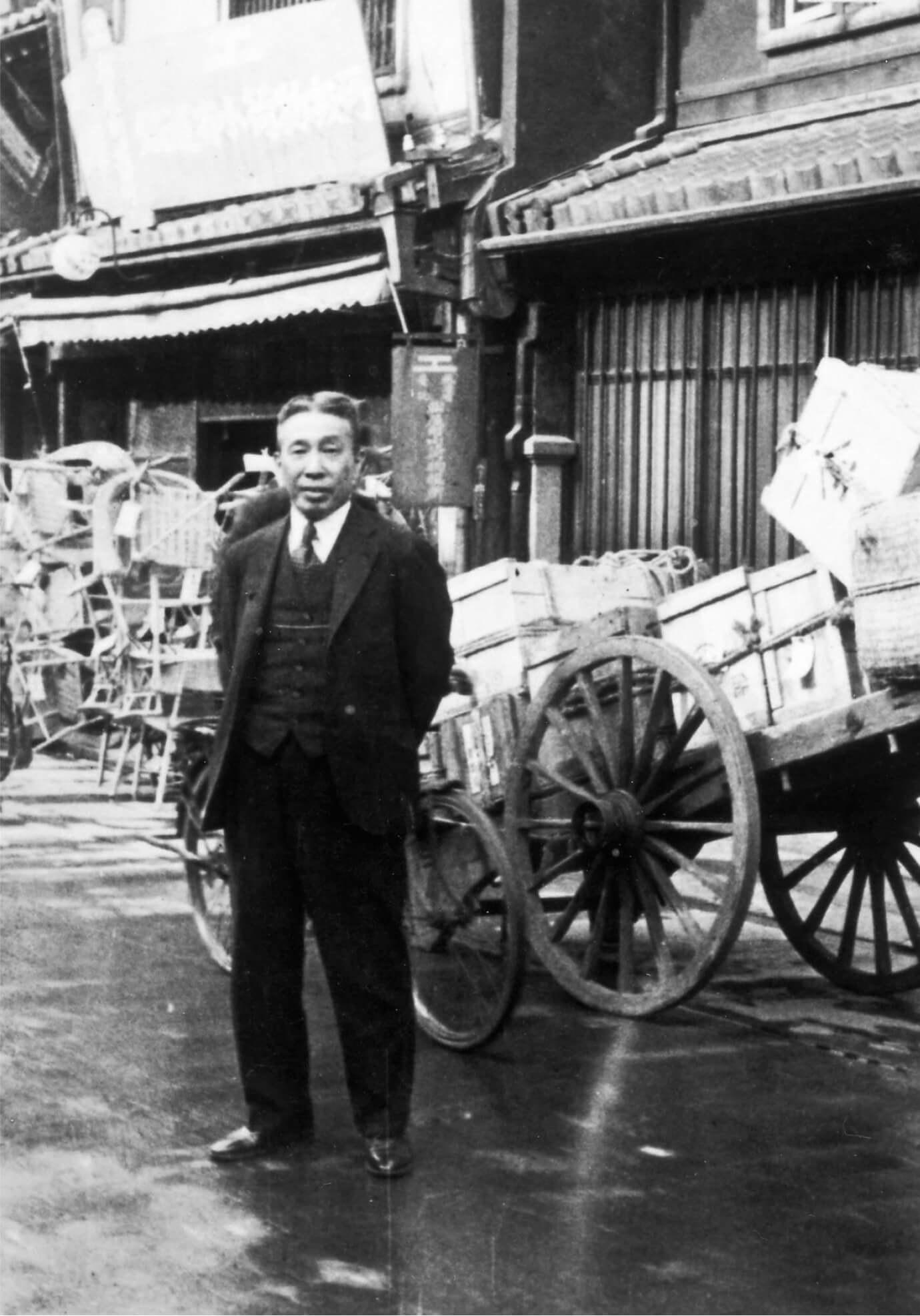 Historic black-and-white photo of Suntory founder Shinjiro Torii in front of wagon carts filled with crates