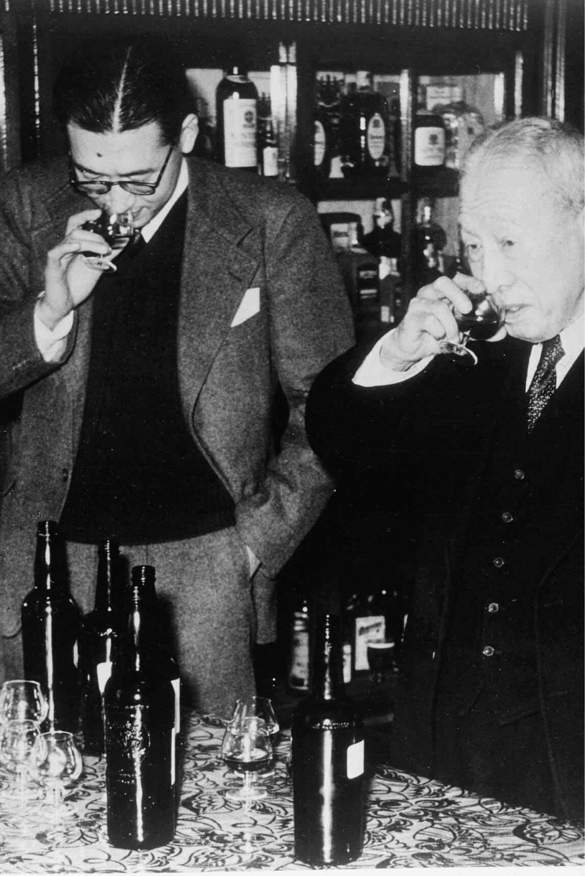Black-and-white photo of Keizo Saji with his father, Suntory founder Shinjiro Torii, sniffing samples of Suntory product